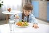 Small girl eating vegetables on plate