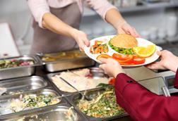 Ein Kind erhält in einer Schulmensa einen Teller mit vollwertigem Essen.