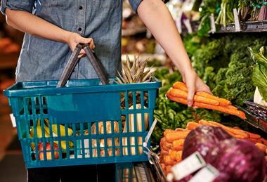 A person picks out carrots at the grocery store to add to their shopping basket