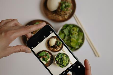 Jemand fotografiert mit dem Handy Teller mit Gemüse, Ansicht von oben