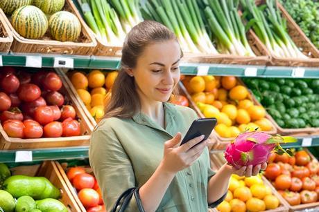 Frau beim Einkaufen, die über ihr Handy weitere Infos zur Drachenfrucht herausfindet.