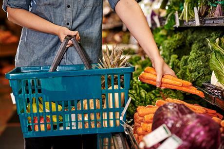 A person picks out carrots at the grocery store to add to their shopping basket
