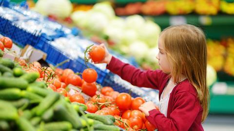 Mädchen greift im Supermarkt bei Tomaten zu