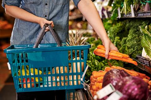 A person picks out carrots at the grocery store to add to their shopping basket