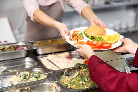 Ein Kind erhält in einer Schulmensa einen Teller mit vollwertigem Essen.