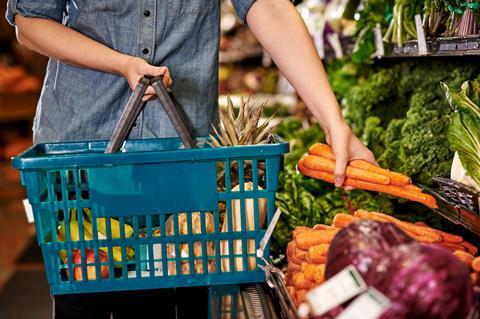 A person picks out carrots at the grocery store to add to their shopping basket