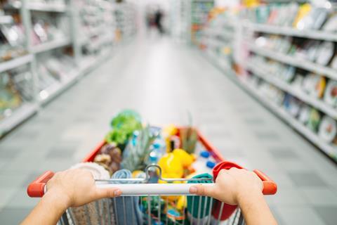 Ein gefüllter Einkaufswagen wird durch die Gänge eines Supermarktes geschoben.